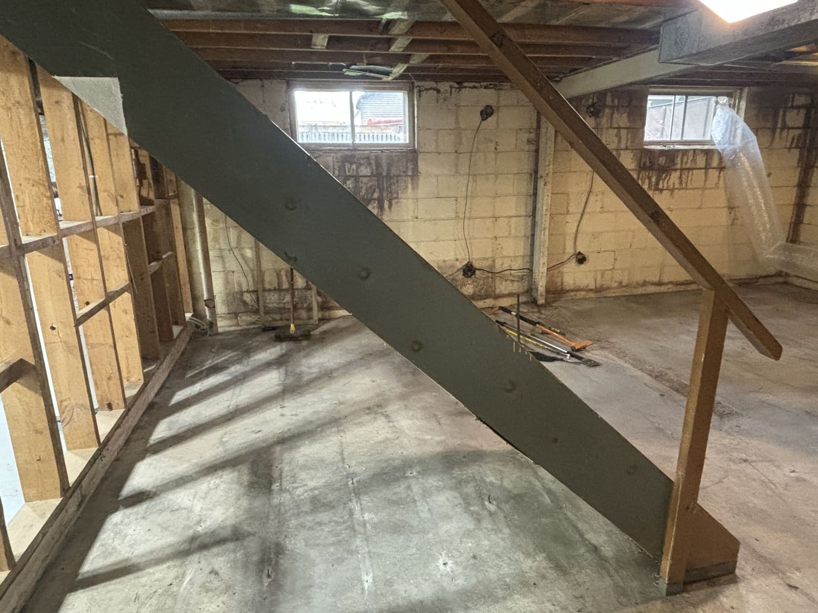 Basement interior taken back to bare structure — exposed joists, block walls, and a swept concrete floor with hand tools staged