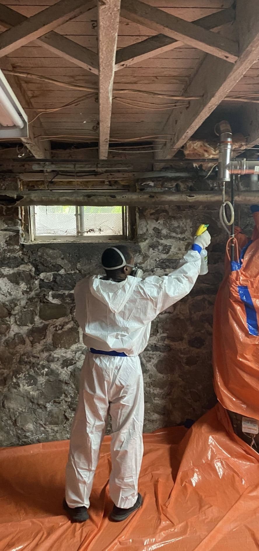 Safeway technician treating a stone foundation wall, with sealed orange waste bags staged beside the work area